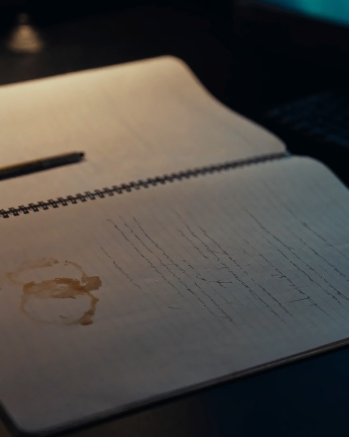An open spiral notebook on a desk, lit low and warm, the writing soft and out of focus